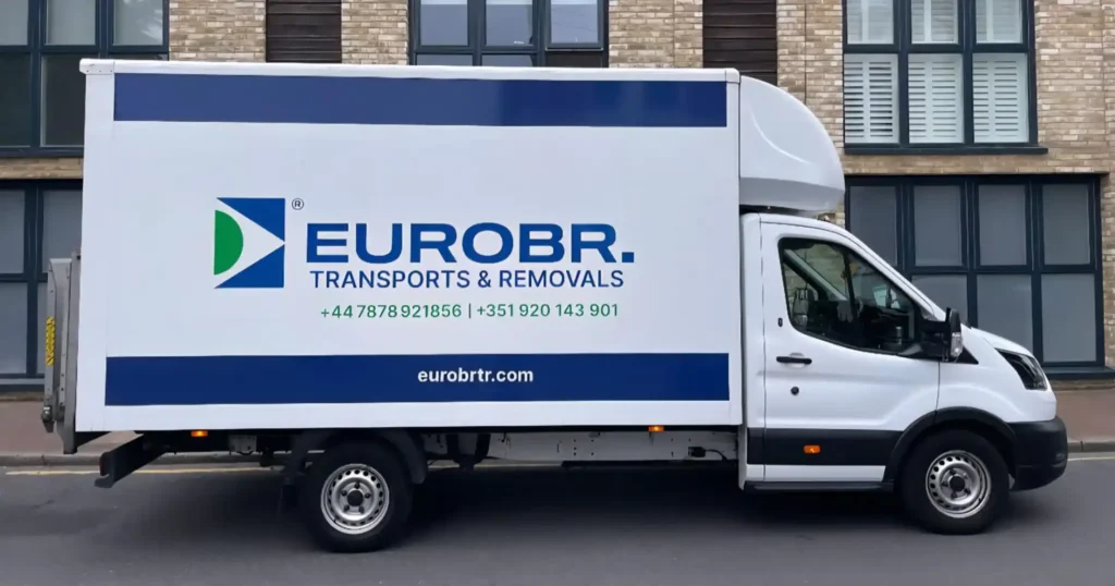 A transport and removal truck with the logo “EUROBR.” and identification “Transports & Removals”, parked in front of a building with windows and a brick facade.